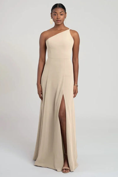 A woman in an elegant one-shoulder chiffon Kora - Jenny Yoo bridesmaid dress from Bergamot Bridal with a thigh-high slit, showcasing a flattering fit and flare.