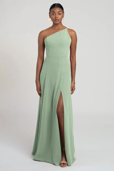 A woman in a flattering fit and flare silhouette one-shoulder Kora - Jenny Yoo Bridesmaid Dress dress with a thigh-high slit from Bergamot Bridal.