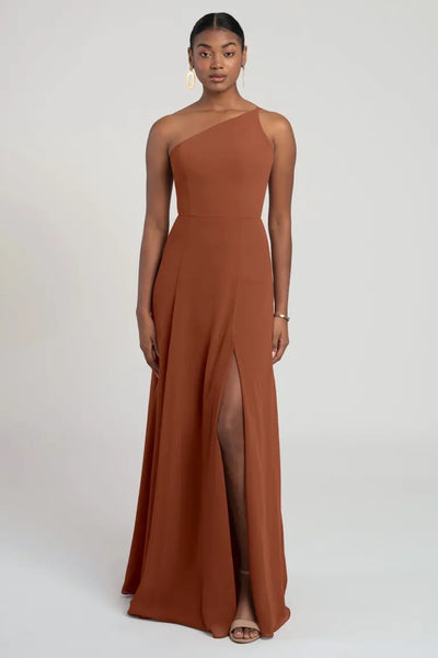 A woman in an elegant one-shoulder chiffon Kora - Jenny Yoo bridesmaid dress by Bergamot Bridal with a thigh-high slit, showcasing a flattering fit and flare silhouette.