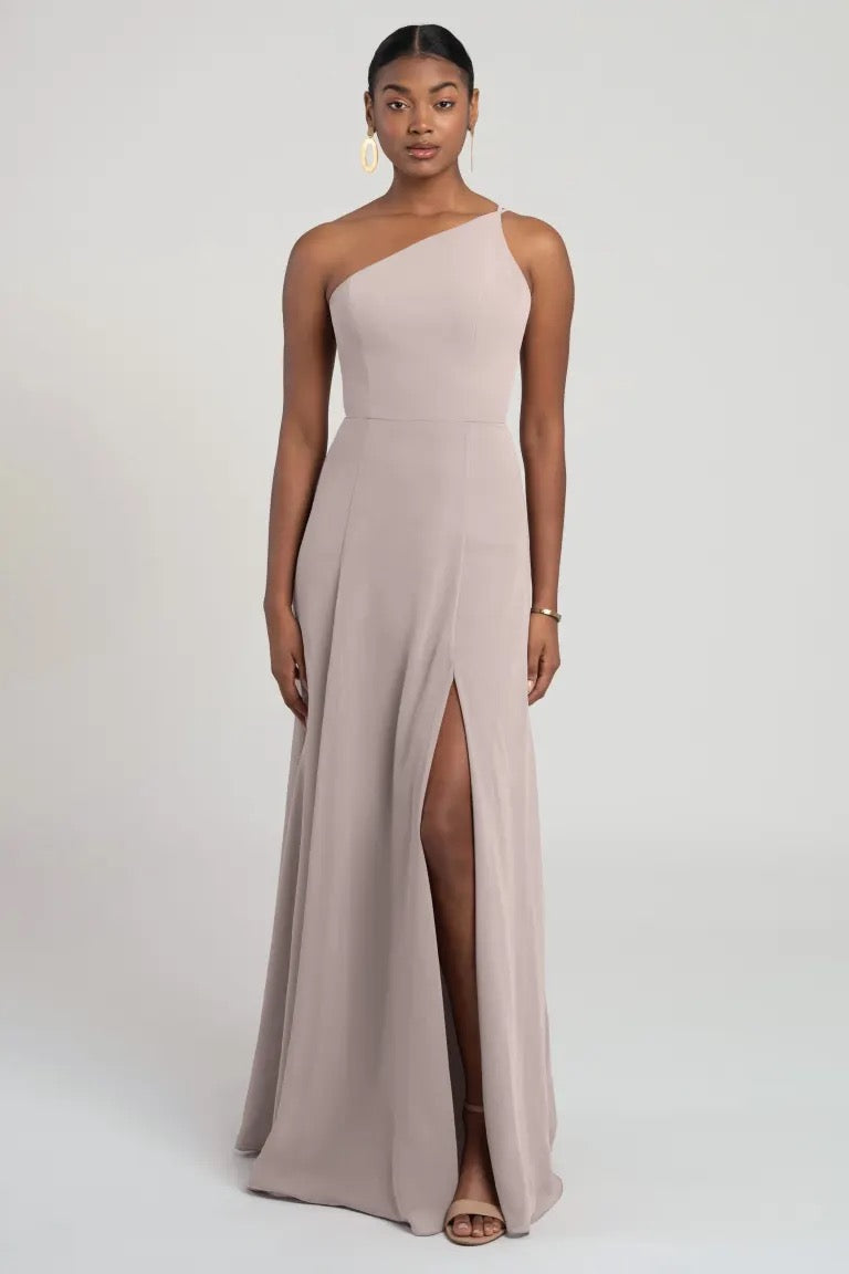A woman standing against a neutral background, wearing an elegant one-shoulder chiffon bridesmaid dress with a flattering fit and flare silhouette, the Kora - Jenny Yoo Bridesmaid Dress from Bergamot Bridal.