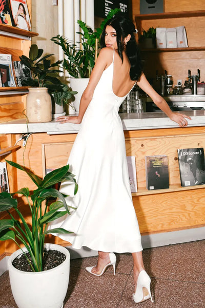 A woman in a wedding dress standing in front of a potted plant, wearing the Callista - Jenny Yoo Little White Dress from Bergamot Bridal.