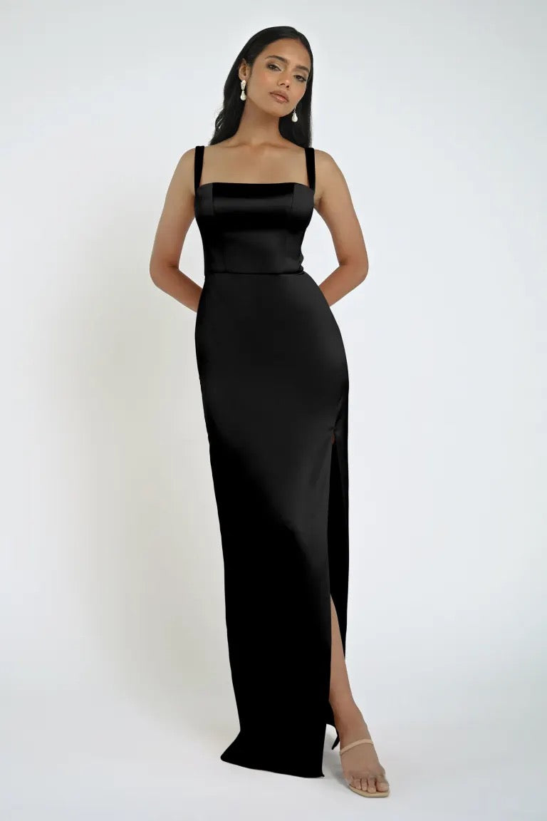 A woman stands posing in the Lowe Bridesmaid Dress by Jenny Yoo from Bergamot Bridal, showcasing a square neckline and a sleek skirt with a slit, paired with high heels.