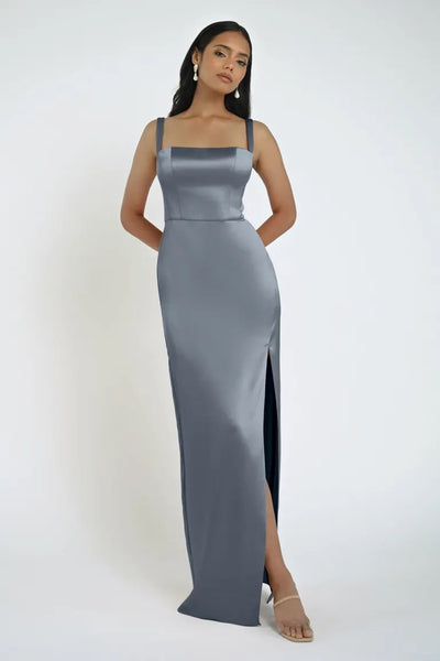 A woman in a gray satin Lowe Bridesmaid Dress by Jenny Yoo, featuring a thigh-high slit and square neckline, poses against a plain white background.