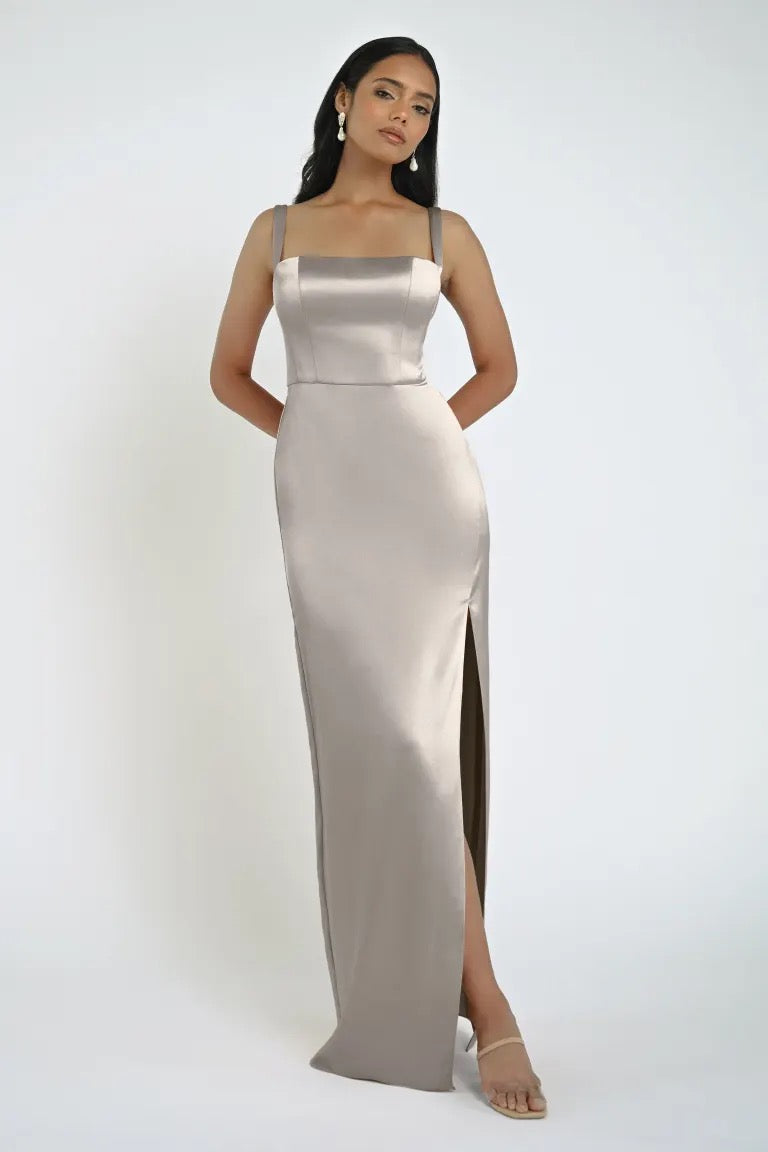 A woman in a sleeveless, floor-length Lowe Bridesmaid Dress by Jenny Yoo with a sleek skirt and square neckline poses against a plain white background.