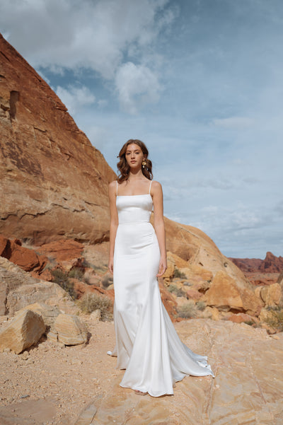 A woman in a Jenny Yoo Wedding Dress gown standing against a desert rock formation from Bergamot Bridal.