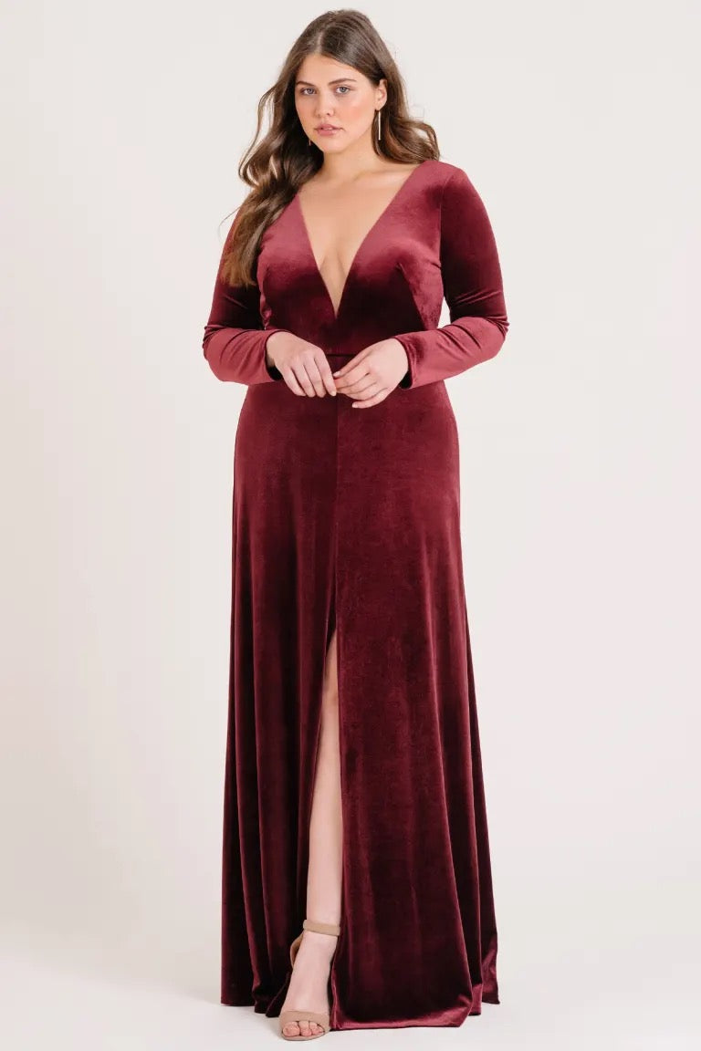 Woman in an elegant long burgundy Malia - Bridesmaid Dress by Jenny Yoo with a slit, posing for a photo from Bergamot Bridal.
