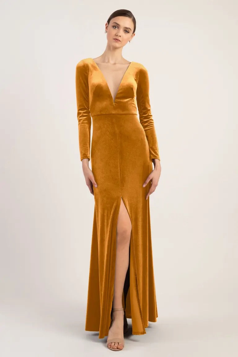A woman posing in an elegant bridesmaid dress, a long-sleeved, deep v-neck, golden Malia - Bridesmaid Dress by Jenny Yoo with a high slit from Bergamot Bridal.