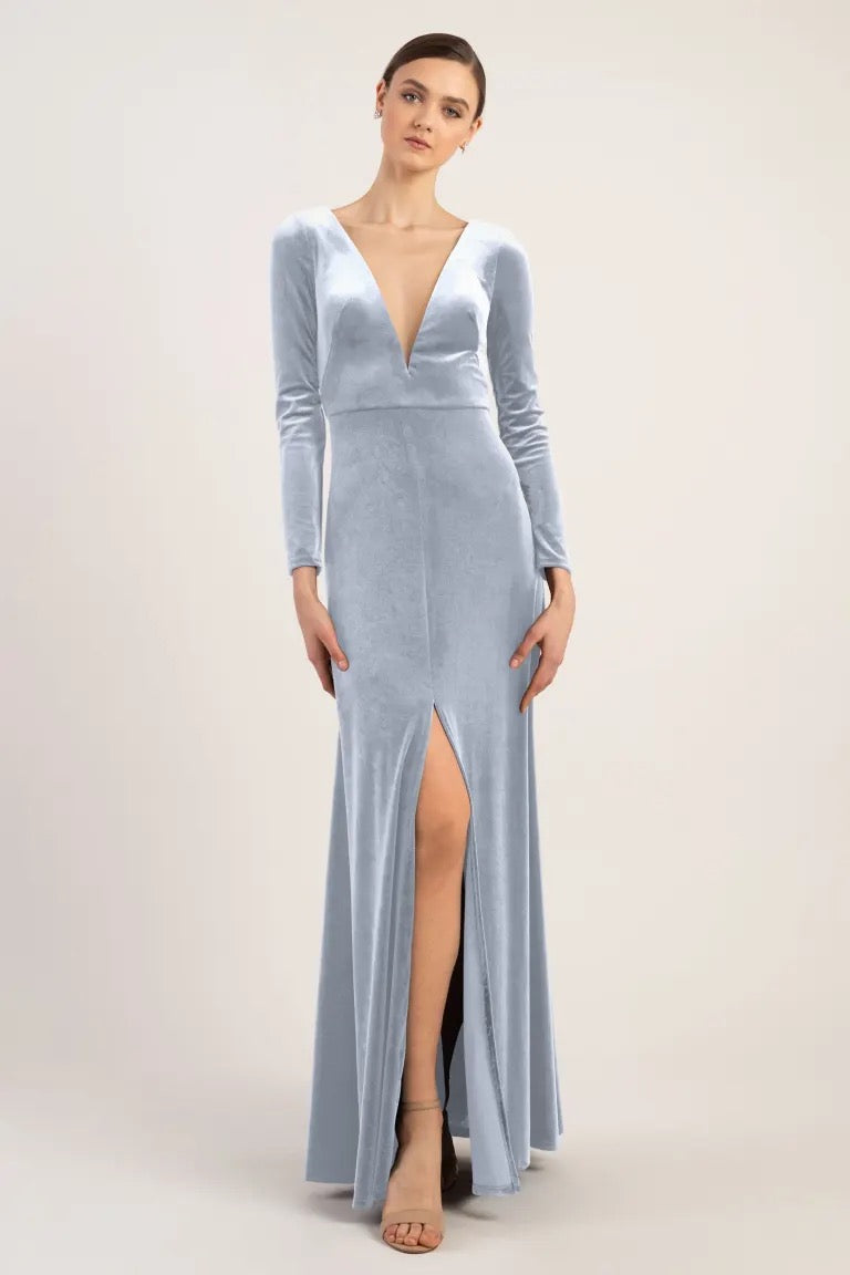 A woman in a luxe velvet Malia - Bridesmaid Dress by Jenny Yoo with a deep v-neckline and a thigh-high slit stands against a neutral background.