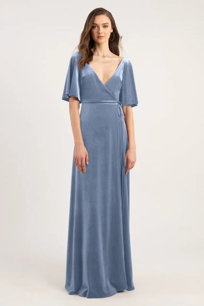 A woman wearing a blue velvet bridesmaid dress with short sleeves and a tied waist, the Marin Bridesmaid Dress by Jenny Yoo from Bergamot Bridal.