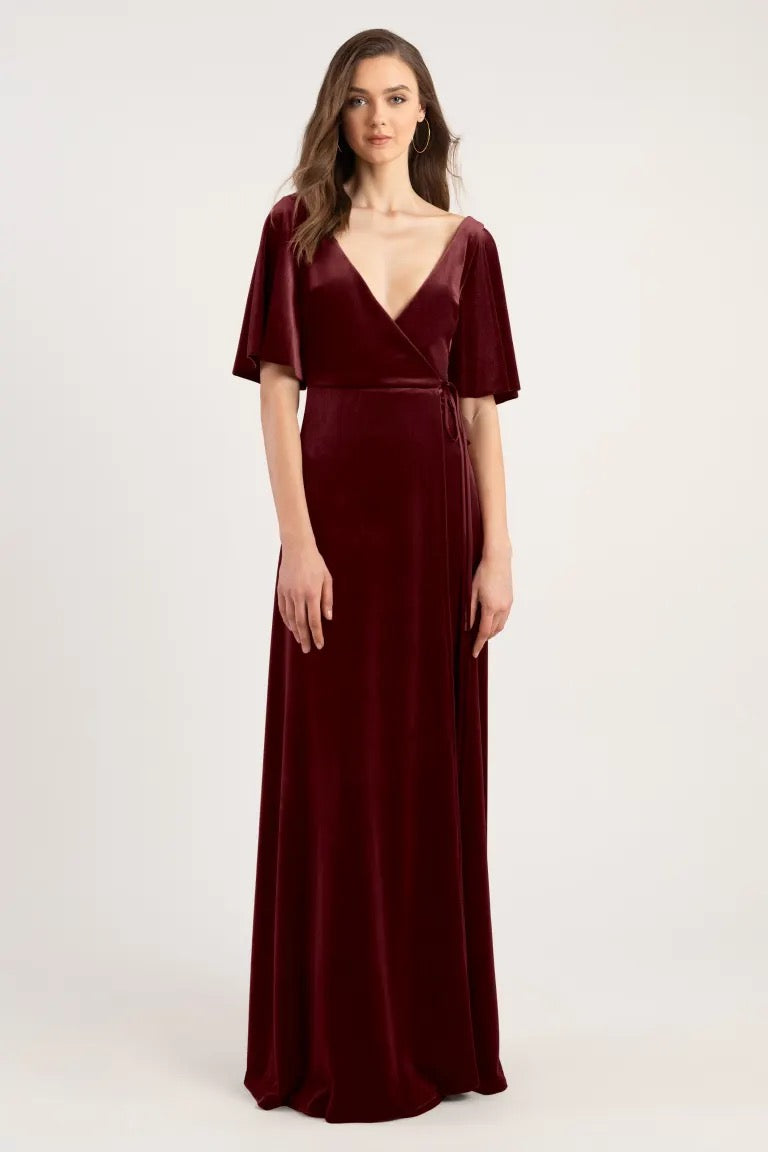 A woman models a floor-length velvet bridesmaid dress with a deep v-neckline, short sleeves, and an adjustable waist tie. 
Product Name: Marin - Bridesmaid Dress by Jenny Yoo 
Brand Name: Bergamot Bridal