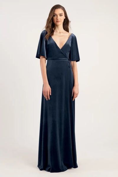 A woman models a navy blue velvet evening gown with a v-neckline and short sleeves. 
Product Name: Marin - Bridesmaid Dress by Jenny Yoo 
Brand Name: Bergamot Bridal