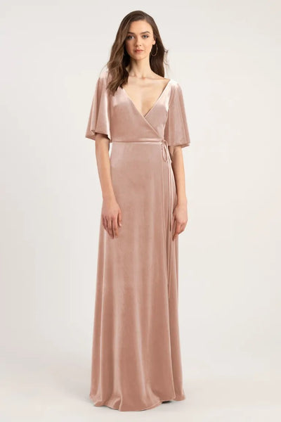 Woman modeling a long blush-colored velvet wrap dress with short sleeves, perfect for a bridesmaid in Marin - Bridesmaid Dress by Jenny Yoo from Bergamot Bridal.