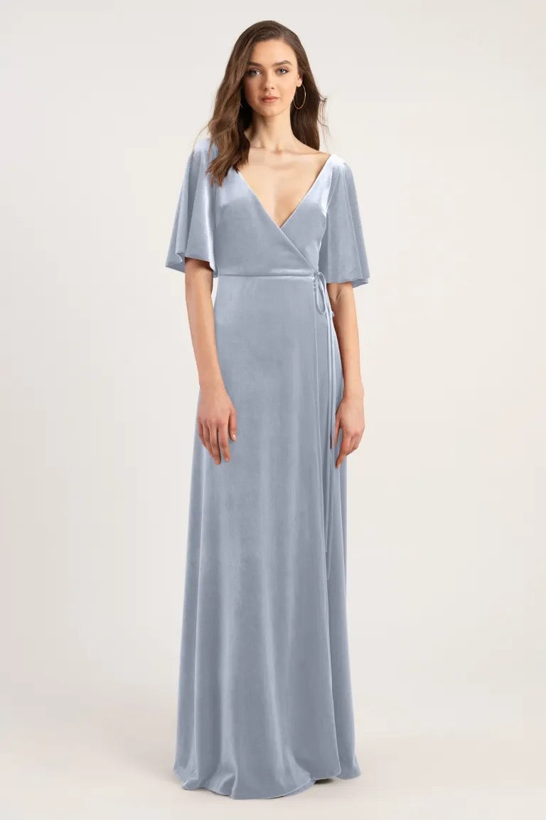 Woman in a light blue velvet v-neck Marin - Bridesmaid Dress by Jenny Yoo standing against a neutral background.