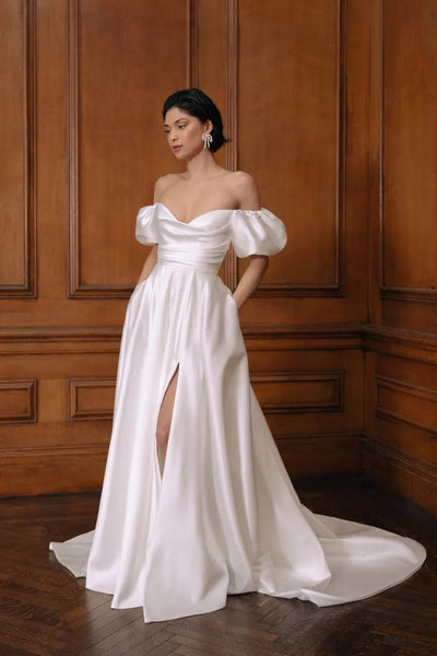 Woman in an elegant Marisol - Jenny Yoo wedding dress by Bergamot Bridal featuring a draped bodice, with a cowl neckline and a long train.