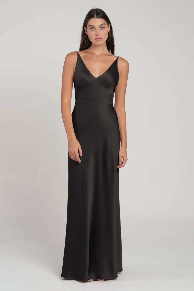 A woman wearing a black sleeveless V-neck evening gown, Marla - Bridesmaid Dress by Jenny Yoo, stands against a neutral background from Bergamot Bridal.