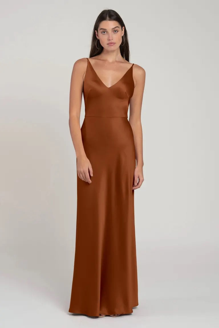 Woman in an elegant brown V-neck, sleeveless Marla - Bridesmaid Dress by Jenny Yoo standing against a neutral background from Bergamot Bridal.