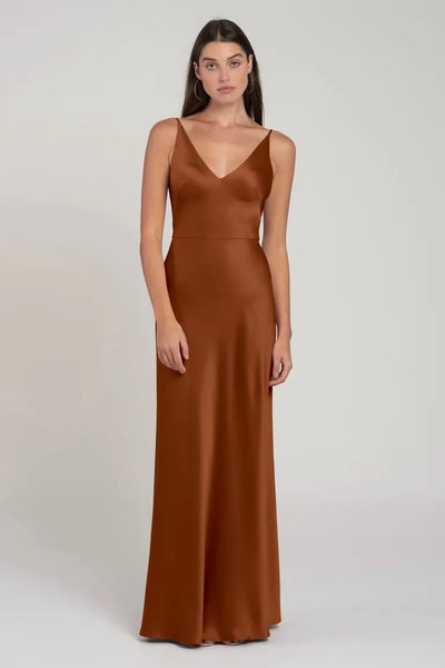 Woman in an elegant brown V-neck, sleeveless Marla - Bridesmaid Dress by Jenny Yoo standing against a neutral background from Bergamot Bridal.