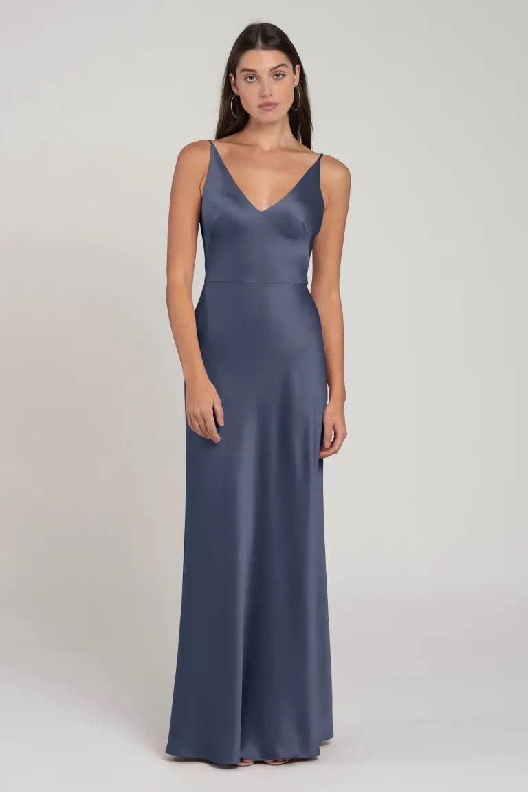 A woman modeling a sleek, blue Marla bridesmaid dress by Jenny Yoo with spaghetti straps and bias cut skirt from Bergamot Bridal.