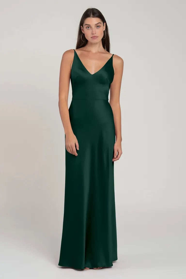 A woman in an elegant Marla - Bridesmaid Dress by Jenny Yoo with a V-neck and spaghetti straps standing against a neutral background.