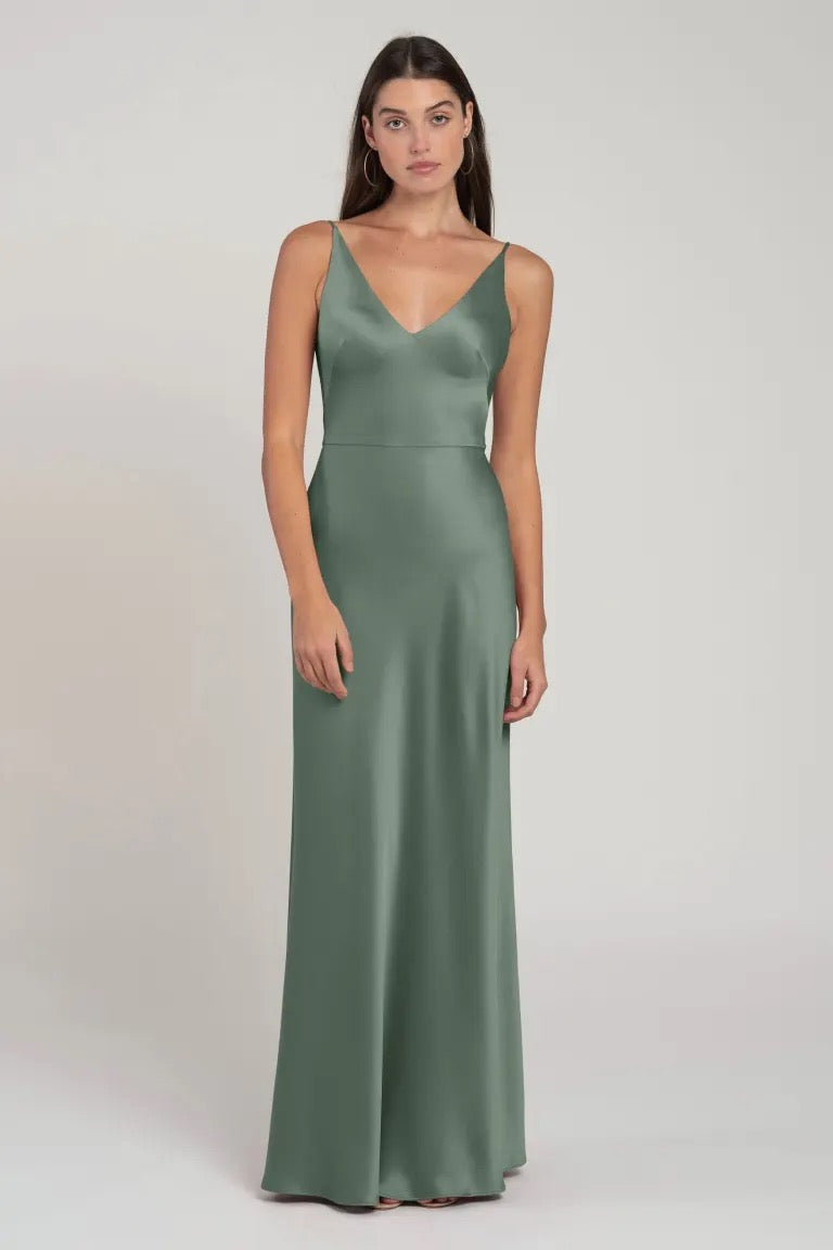 A woman posing in an elegant sage green satin Marla bridesmaid dress by Jenny Yoo with a V-neck from Bergamot Bridal.