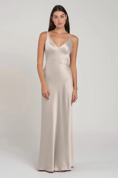 A woman in an elegant, sleeveless, satin Marla bridesmaid dress by Jenny Yoo with a bias-cut skirt stands against a neutral background.