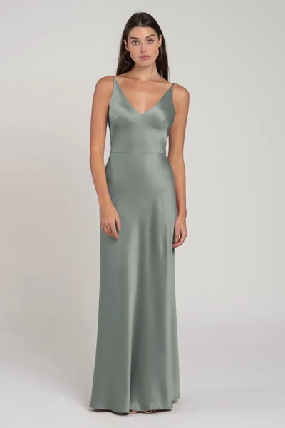 A woman in a sleek, sage green Marla - Bridesmaid Dress by Jenny Yoo stands against a neutral background.