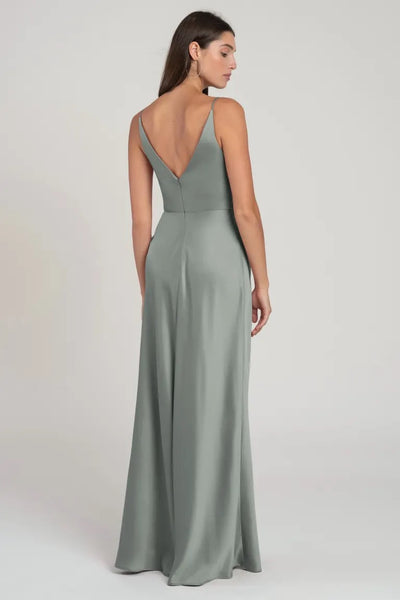 Woman in an elegant, bias-cut, sage green satin Marla bridesmaid dress by Jenny Yoo from Bergamot Bridal looking over her shoulder.