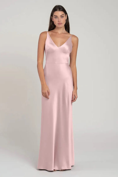 A woman models a long pale pink satin bridesmaid dress with spaghetti straps and a V-neckline, the Marla - Bridesmaid Dress by Jenny Yoo from Bergamot Bridal.