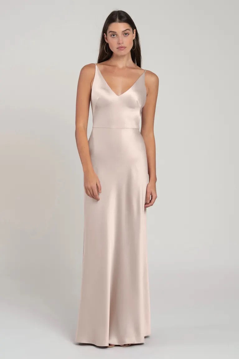 Woman posing in a sleek, satin Marla bridesmaid dress by Jenny Yoo with a bias cut skirt and a V-neck in cream color from Bergamot Bridal.
