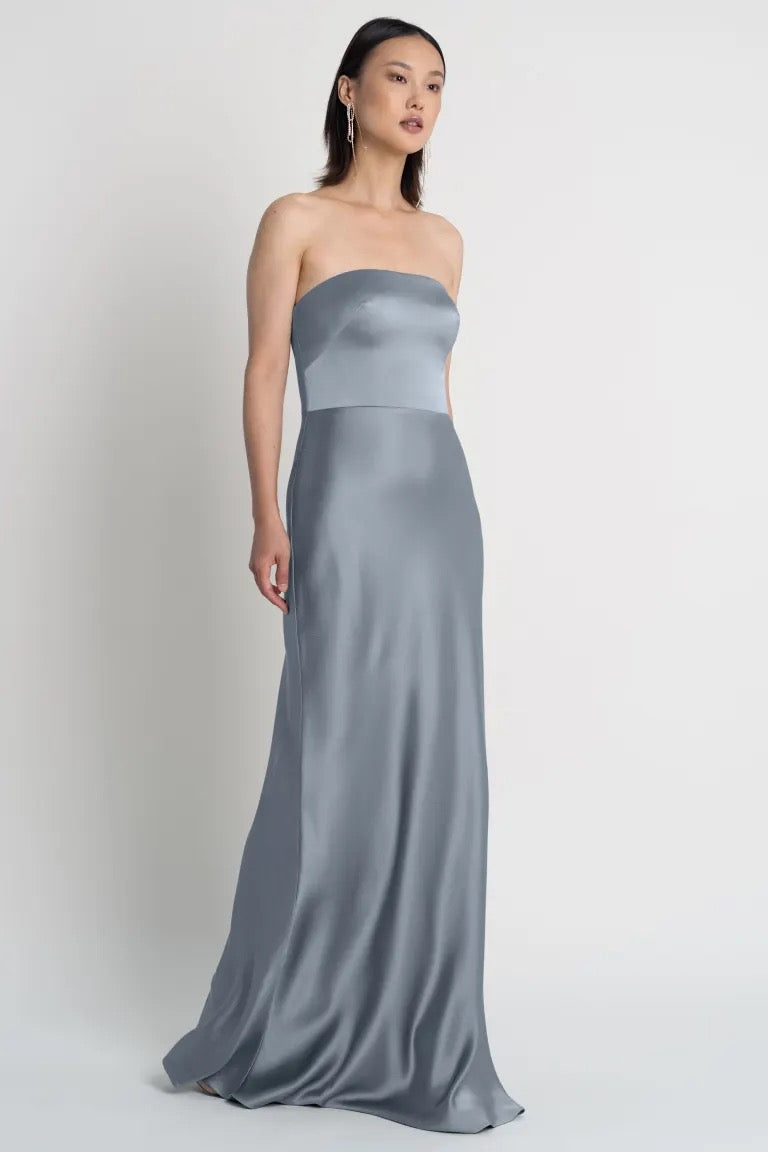 Woman modeling the Melody - Bridesmaid Dress by Jenny Yoo, a strapless grey evening gown with a bias-cut skirt from Bergamot Bridal.