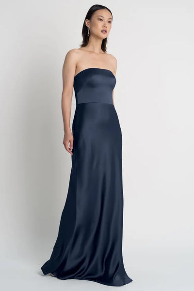 A woman posing in an elegant strapless neckline navy blue Melody satin dress by Jenny Yoo, Bergamot Bridal.