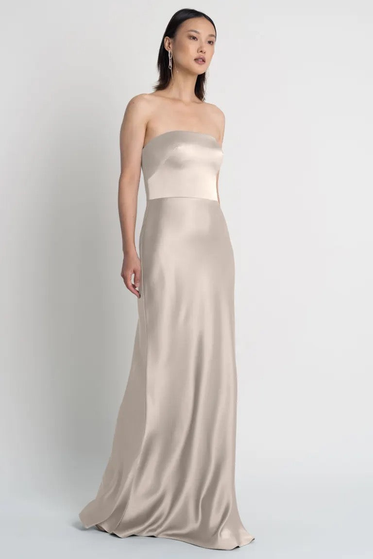 A woman modeling a strapless Melody bridesmaid dress by Jenny Yoo in a neutral shade with a bias-cut skirt from Bergamot Bridal.