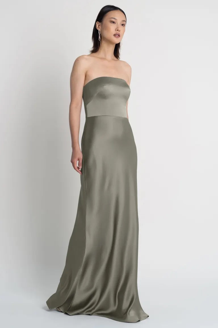 A woman in a strapless neckline, olive green Melody satin dress standing against a neutral background. 
Product Name: Melody - Bridesmaid Dress by Jenny Yoo
Brand Name: Bergamot Bridal