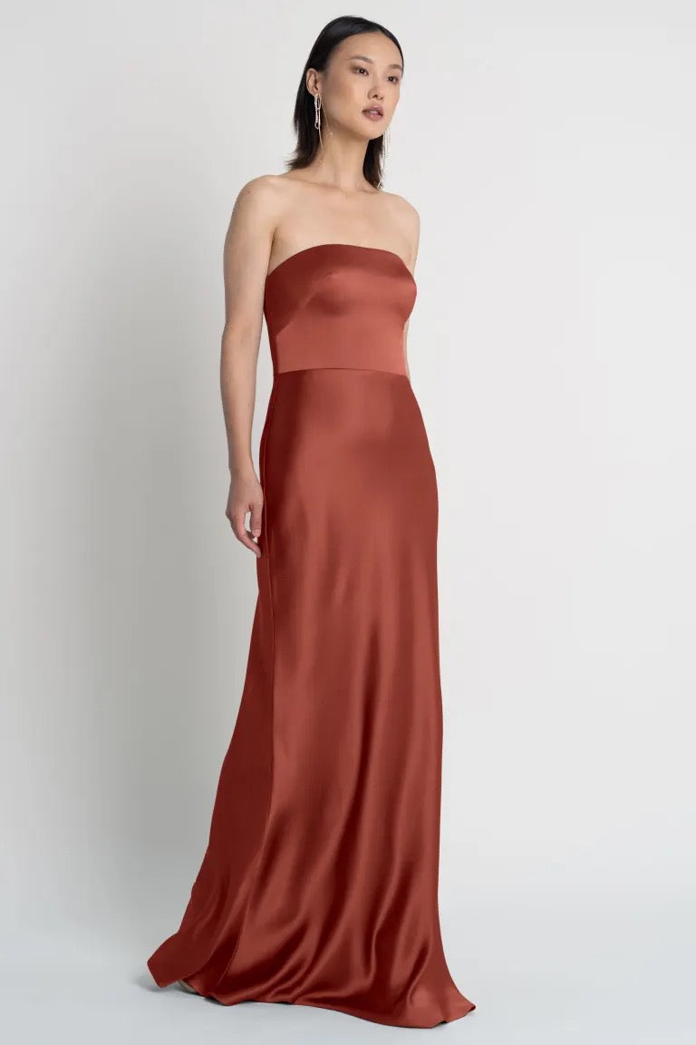 Woman in an elegant strapless rust-colored Melody - Bridesmaid Dress by Jenny Yoo satin dress from Bergamot Bridal.