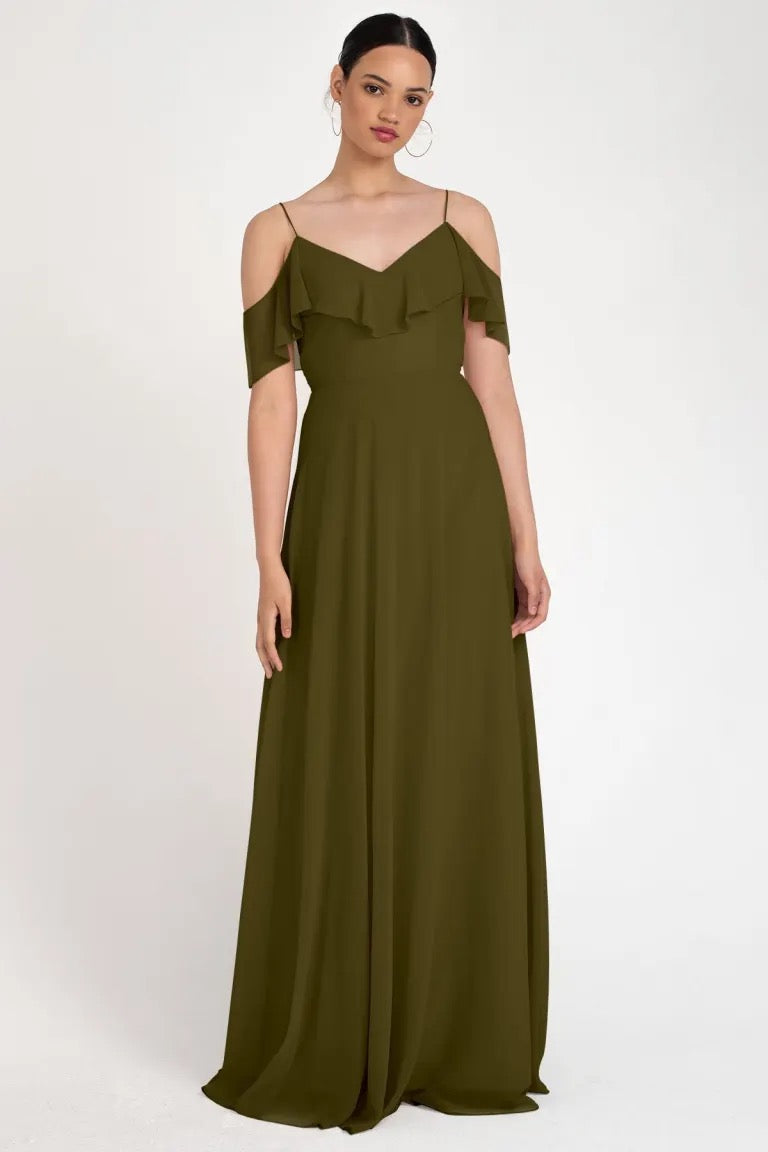 A woman in the Mila - Bridesmaid Dress by Jenny Yoo, designed by Bergamot Bridal, in an elegant olive green off-the-shoulder gown with ruffle detailing and a circle skirt.