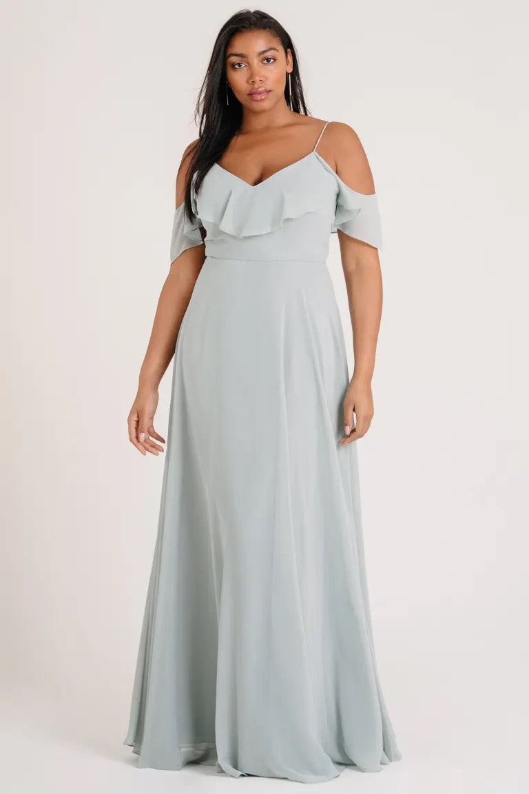 Woman in a light blue off-the-shoulder Mila - Bridesmaid Dress by Jenny Yoo standing against a neutral background.