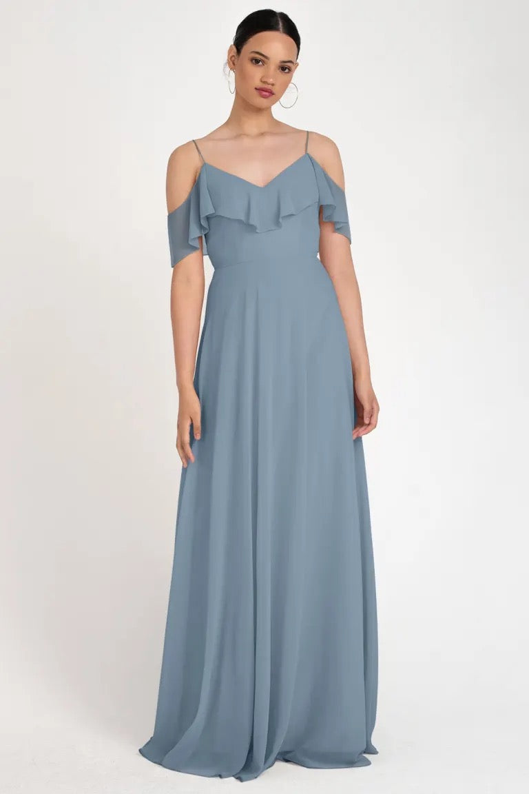 Woman posing in an elegant blue off-the-shoulder neckline evening gown with a circle skirt silhouette, the Mila bridesmaid dress by Jenny Yoo from Bergamot Bridal.