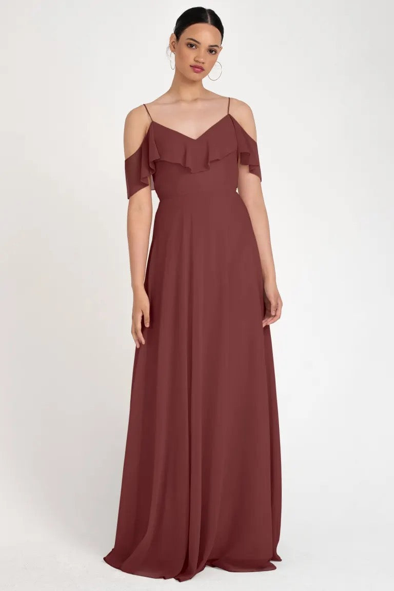 Woman posing in an elegant off-the-shoulder burgundy evening gown, Mila - Bridesmaid Dress by Jenny Yoo, store sample size 22 from Bergamot Bridal.