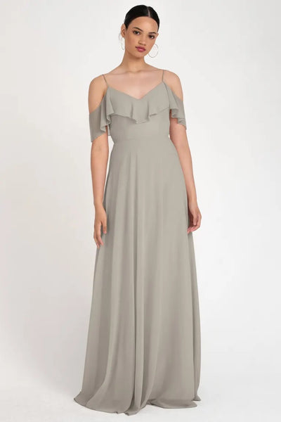 Woman in a Mila - Bridesmaid Dress by Jenny Yoo from Bergamot Bridal, with an off-the-shoulder neckline and cold-shoulder sleeves, standing against a plain background.