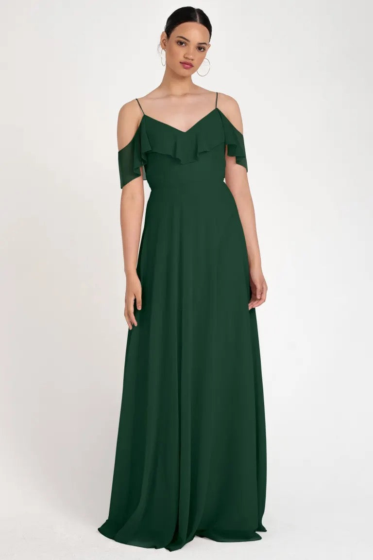 Woman in an elegant green off-the-shoulder gown with a circle skirt silhouette, posing against a neutral background wearing the Mila Bridesmaid Dress by Jenny Yoo from Bergamot Bridal.