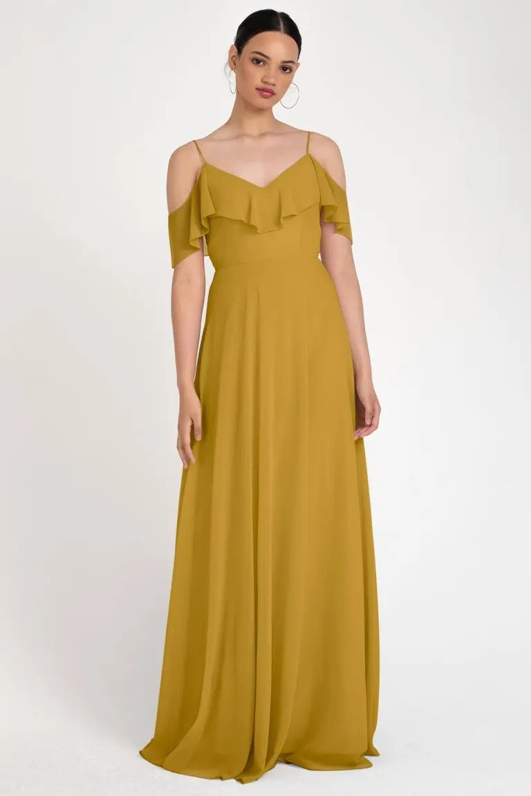 Woman posing in an elegant mustard Mila bridesmaid dress by Jenny Yoo with off-the-shoulder ruffle details from Bergamot Bridal.