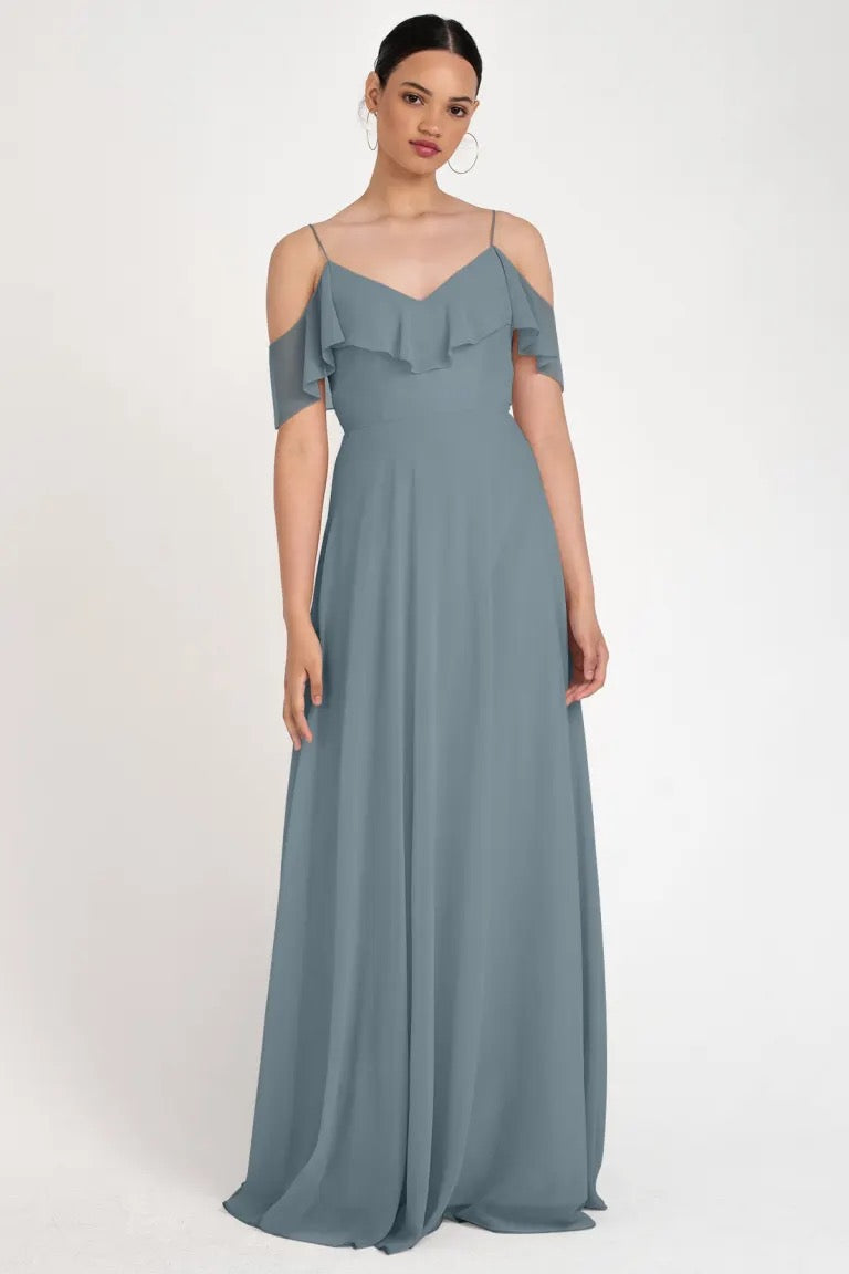 A woman modeling an elegant gray evening gown with an off-the-shoulder neckline, the Mila - Bridesmaid Dress by Jenny Yoo from Bergamot Bridal.