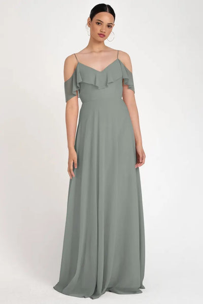 A woman standing and posing in a Mila - Bridesmaid Dress by Jenny Yoo in a gray off-the-shoulder evening gown with a circle skirt silhouette from Bergamot Bridal.
