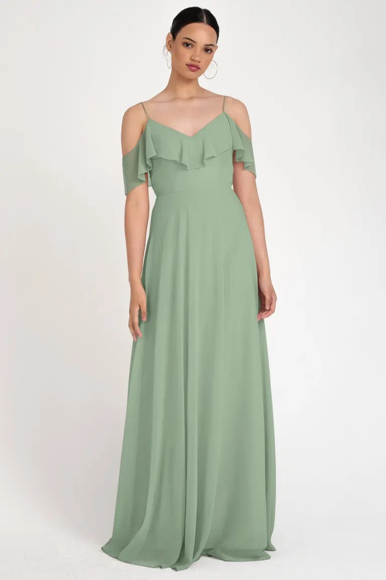 A woman wearing an elegant sage green Mila - Bridesmaid Dress by Jenny Yoo with an off-the-shoulder neckline and ruffle details in a store sample size 22 at Bergamot Bridal.