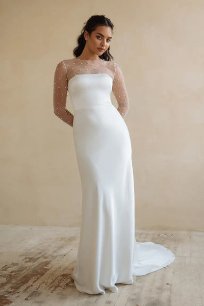 Woman posing in an elegant Bergamot Bridal Jenny Yoo wedding dress with sheer dotted sleeves, embellished with pearls.