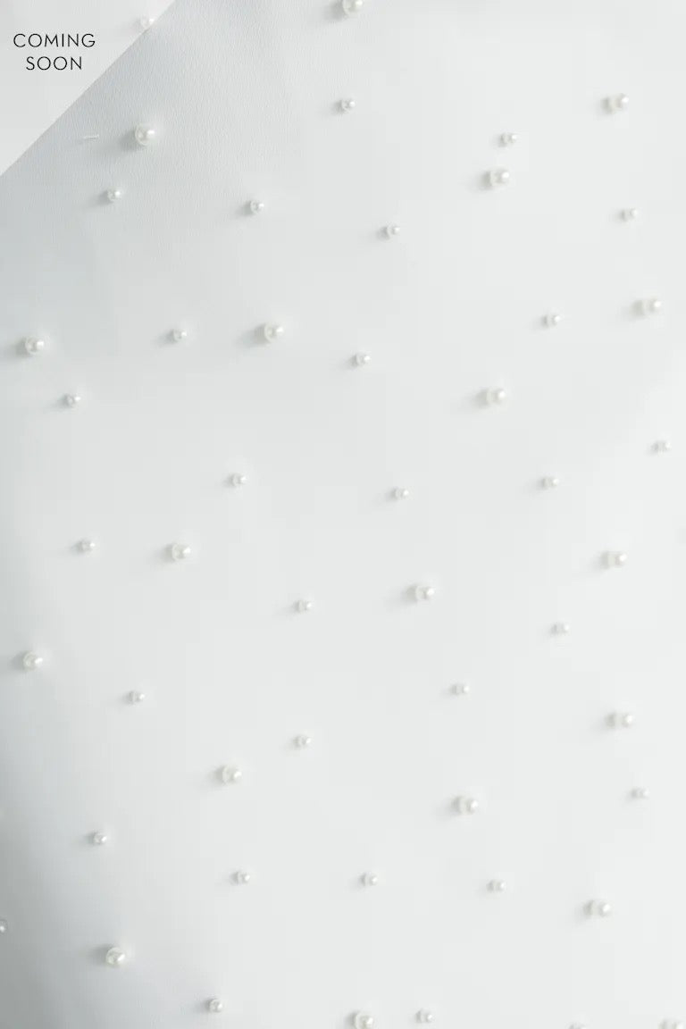 The Oksana - Jenny Yoo Little White Dress by Bergamot Bridal features white luxe stretch crepe with evenly spaced pearl beads. "COMING SOON" is shown in the upper left corner.