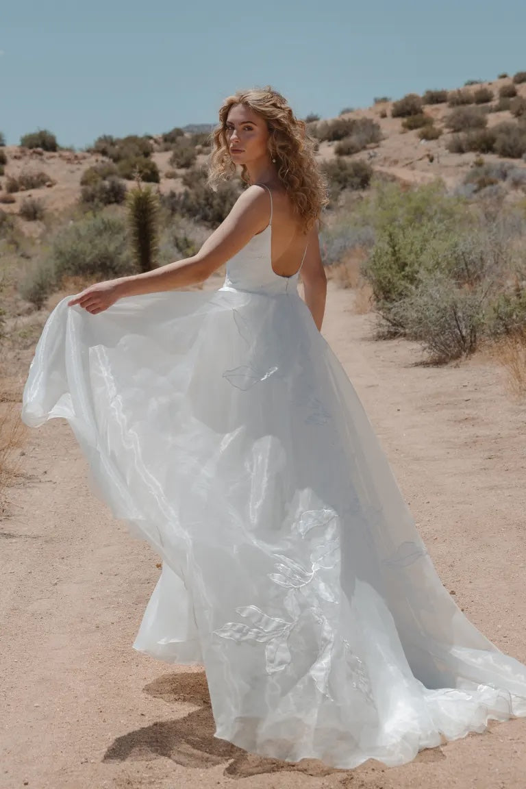 Woman in dramatic Abernathy - Jenny Yoo Wedding Dress and floral organza applique standing in a desert setting by Bergamot Bridal.