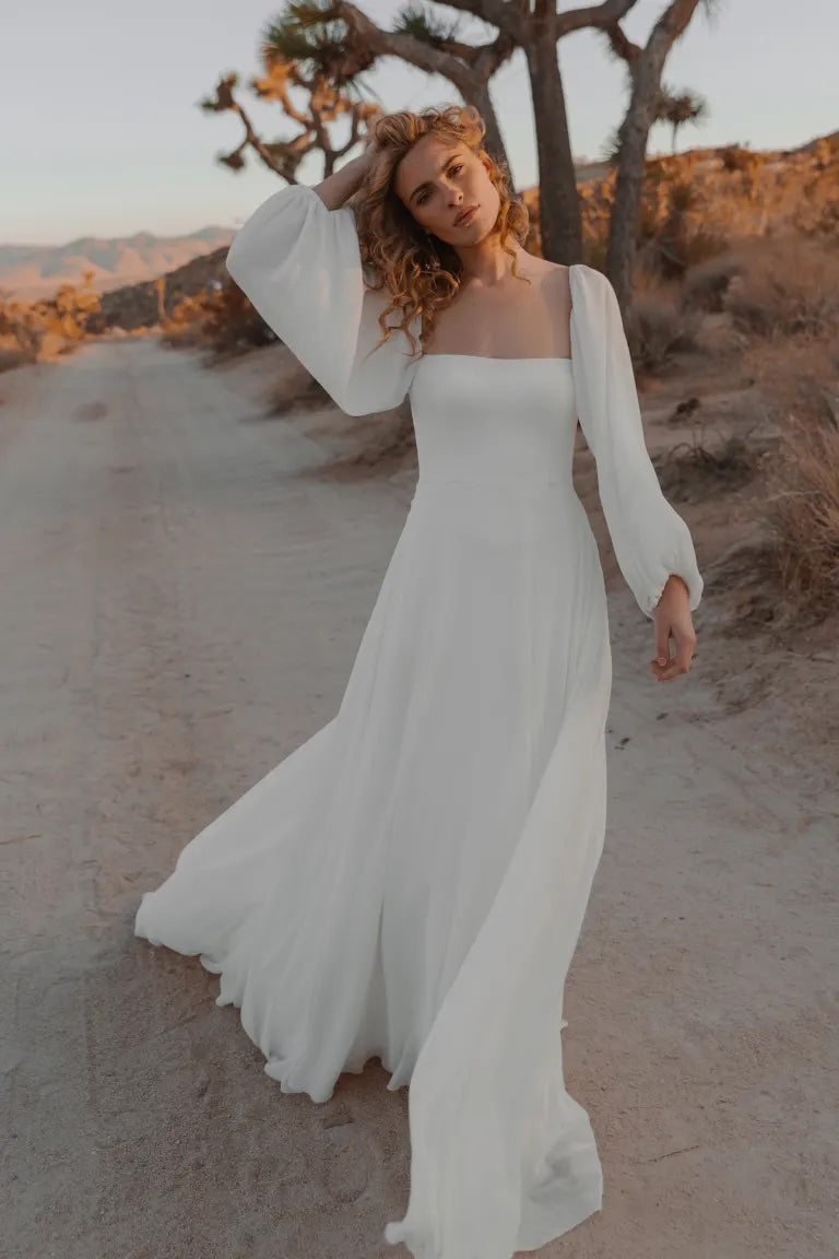 Woman in a white chiffon wedding dress posing on a desert path at sunset wearing the Louise - Jenny Yoo Wedding Dress from Bergamot Bridal.