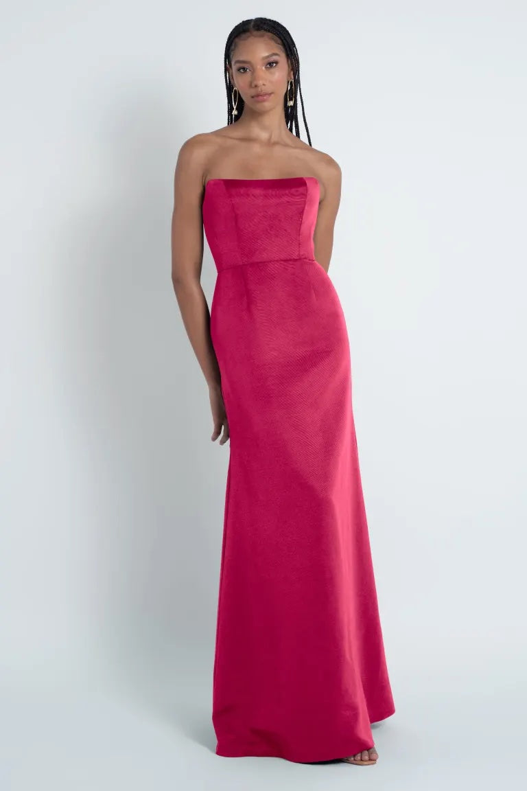 Woman in a Jenny Yoo Bridesmaid Dress designed with Luxe Faille fabric, a strapless pink gown standing against a white background from Bergamot Bridal.