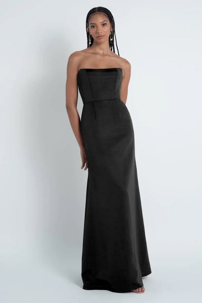 A woman in a strapless black Bergamot Bridal - Jenny Yoo Bridesmaid Dress stands against a light gray background.